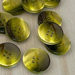 May include: A collection of ten green and brown buttons with four holes each. The buttons have a glossy finish and a gradient color effect.