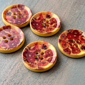 May include: Five yellow wooden buttons with a red and yellow floral design. Each button has four holes.