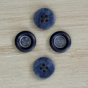 May include: Four navy blue buttons with four holes each. Two buttons have a silver ring around the holes. The buttons are arranged in a square pattern on a light wood surface.
