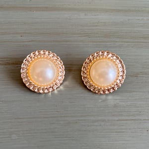 May include: A pair of gold-tone earrings with a pearl center and a decorative, textured border.