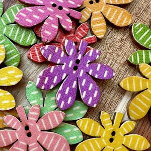 May include: Assortment of colorful wooden flower-shaped buttons with white stripes. The buttons are in various shades of pink, purple, yellow, and green.