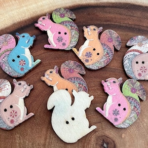 May include: Set of ten wooden buttons featuring a squirrel design. The buttons are painted in various colors, including pink, blue, orange, and brown. Each button has a unique pattern and two holes for sewing.