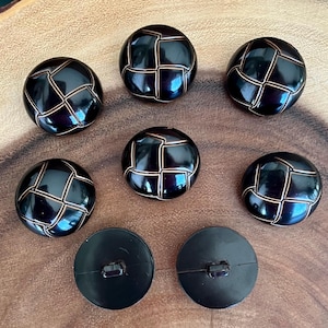 May include: Eight black buttons with a woven design in a light brown color. The buttons are round and have a shiny finish.