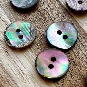 May include: A set of six iridescent mother-of-pearl buttons with two holes each. The buttons are round and have a smooth, polished finish.
