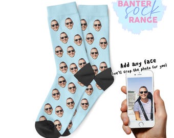 Könnte beinhalten: Hellblaue Socken mit einem sich wiederholenden Muster eines lächelnden Gesichts mit Sonnenbrille. Die Socken haben schwarze Fersen und Zehen. Der Text "BANTER SOCK RANGE" befindet sich oben rechts. Ein Telefon zeigt ein Gesicht.