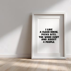 Könnte beinhalten: Ein gerahmter Druck mit dem Text "I LIKE A CLEAN HOUSE, PICKY BITS, THE WORD CUNT AND ABOUT 4 PEOPLE." Der weiße Rahmen steht an einer weißen Wand und einem Holzboden.