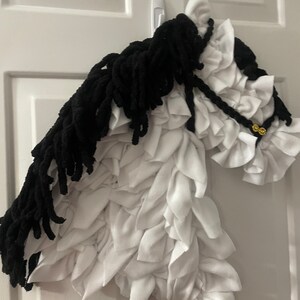 May include: A white and black horse head made of fabric. The horse has a black mane and tail, and the body is made of white fabric with a ruffled texture.