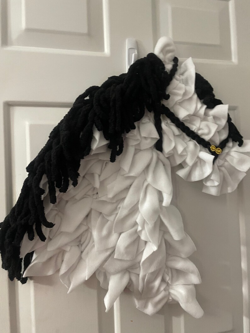 May include: A white and black horse head made of fabric. The horse has a black mane and tail, and the body is made of white fabric with a ruffled texture.