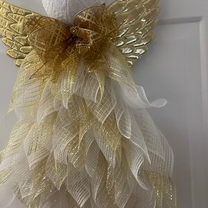 May include: A white angel Christmas decoration with gold wings and a gold bow. The angel is made of mesh and has a white head with a gold trim.