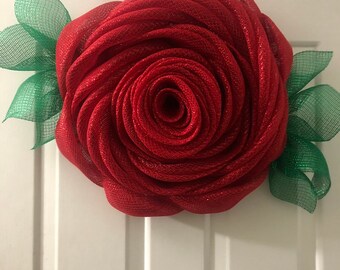 May include: A large red mesh rose wreath with green mesh leaves. The wreath is hanging on a white door.