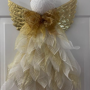 May include: A white angel figurine with gold wings and a gold bow. The angel is decorated with white and gold mesh.