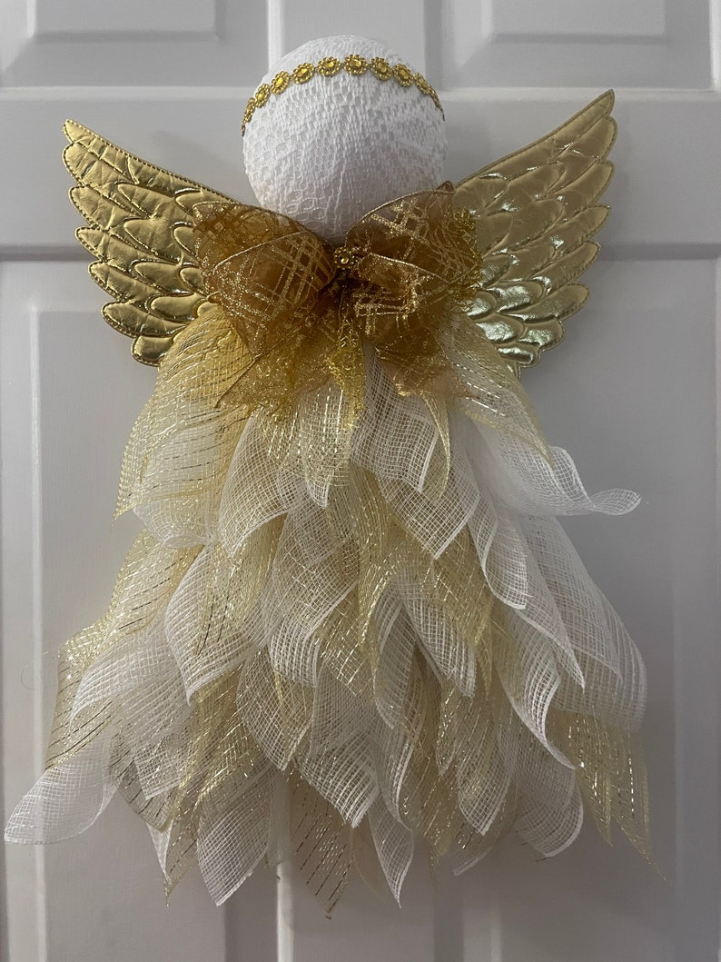 May include: A white angel figurine with gold wings and a gold bow. The angel is decorated with white and gold mesh.