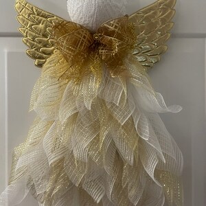 May include: A white angel figurine with gold wings and a gold bow. The angel is decorated with white and gold mesh.