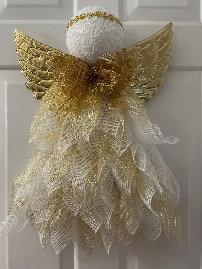 May include: A white angel figurine with gold wings and a gold bow. The angel is decorated with white and gold mesh.