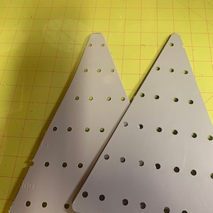 May include: Two gray plastic triangle earring display stands with holes for earrings. The stands are on a yellow grid surface.