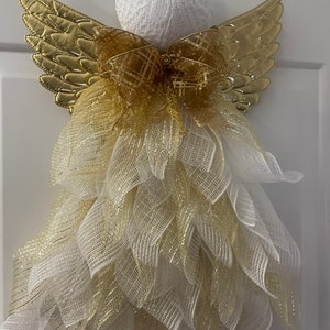 May include: A white angel-shaped Christmas decoration with gold wings and a gold and white bow. The angel is made of mesh and has a white lace head.