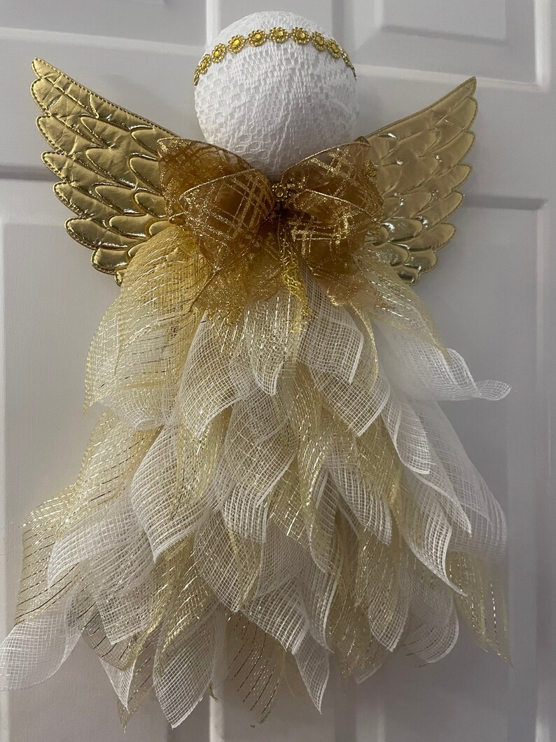 May include: A white angel-shaped Christmas decoration with gold wings and a gold and white bow. The angel is made of mesh and has a white lace head.