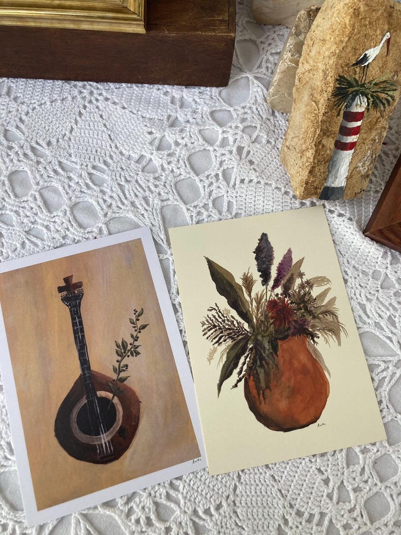 May include: Two framed prints, one with a black and white illustration of a musical instrument, and the other with a watercolor painting of a bouquet of flowers in a terracotta pot.