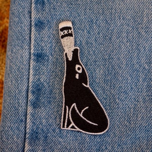 May include: Black and white embroidered patch of a wolf howling at a bottle with the text "XXX" on it.