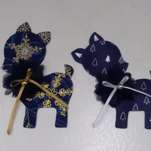 Puede incluir: Dos adornos de reno azules y dorados con lazos de tul negro y cinta dorada y blanca. El reno de la izquierda tiene un patrón de copo de nieve y el reno de la derecha tiene un patrón de árbol blanco.
