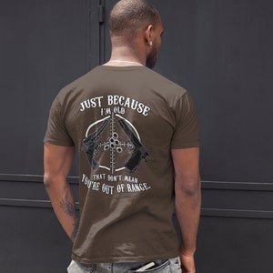 May include: Brown t-shirt with a white graphic print that says "Just because I'm old that don't mean you're out of range." The graphic also features two guns and a target.