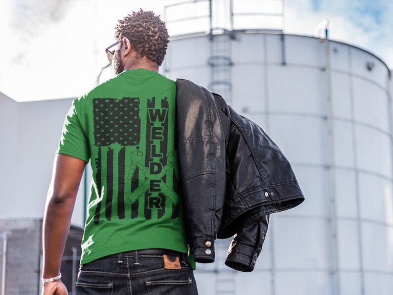 Puede incluir: Camiseta verde con un dise&ntilde;o de bandera estadounidense en blanco y negro y la palabra "WELDER" con herramientas de soldadura cruzadas.