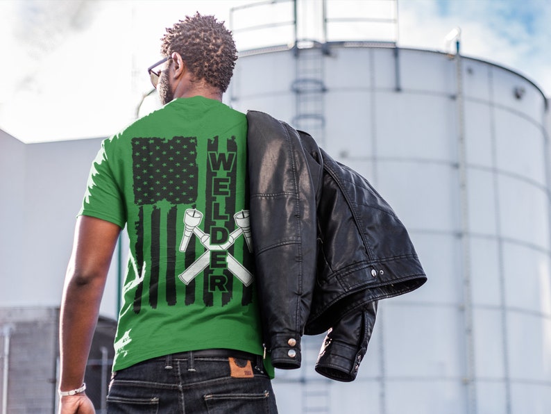 Puede incluir: Camiseta verde con un dise&ntilde;o de bandera estadounidense en blanco y negro y la palabra "WELDER" con antorchas de soldadura cruzadas.