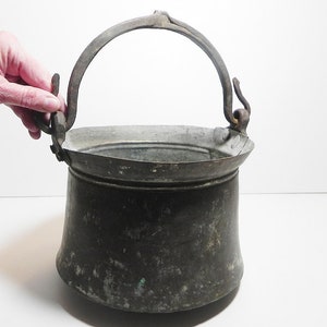 May include: An antique copper bucket with a wrought iron handle. The bucket is tarnished and has a rustic look.