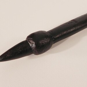 May include: A close-up of a dark brown metal spike with a rounded tip. The spike is on a white background.