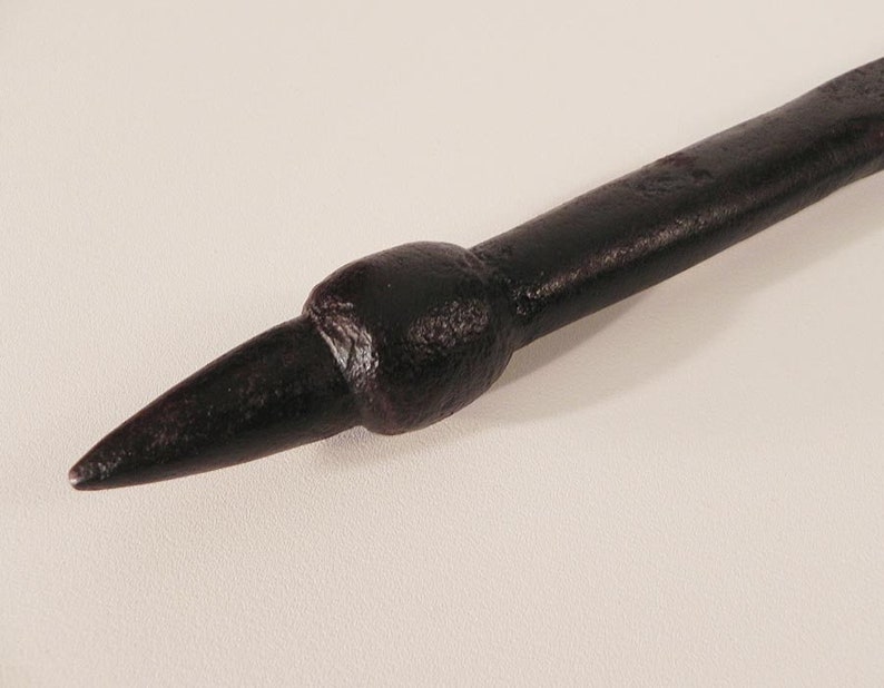 May include: A close-up of a dark brown metal spike with a rounded tip. The spike is on a white background.