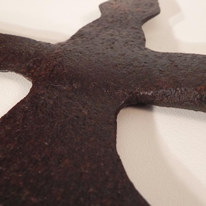 May include: Close-up of a rusty, dark brown metal axe head with a curved blade. The axe head is shaped like a cross with a pointed tip.