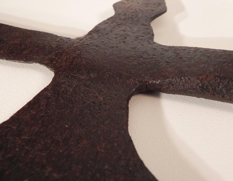 May include: Close-up of a rusty, dark brown metal axe head with a curved blade. The axe head is shaped like a cross with a pointed tip.
