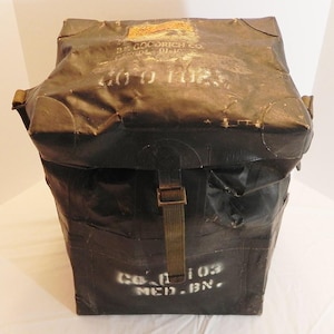 May include: A vintage, dark brown, rectangular bag with a flap closure and a buckle strap. The bag has visible wear and tear, with faded white lettering and the text "B.F. GOODRICH CO." and "CO. 103 MED. BN."