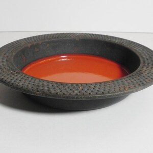 May include: A black cast iron ashtray with a red interior. The ashtray has a textured rim.