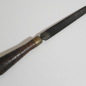 May include: A vintage metal file with a wooden handle. The file has a coarse, rough surface and is used for shaping metal.