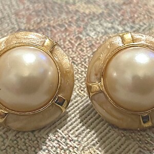 May include: A pair of gold tone earrings with a faux pearl center and a cream colored shell-like design.