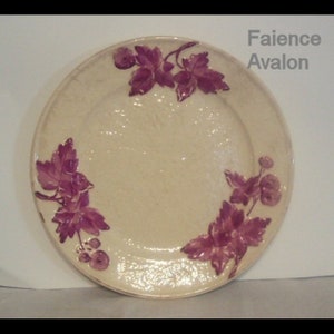 May include: A white ceramic plate with a pink floral design. The plate has a raised rim and a smooth surface. The floral design features leaves and berries.