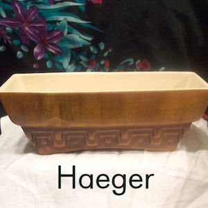 以下が含まれることがあります： 幾何学模様の茶色の陶器製のプランター。プランターは長方形で、わずかに盛り上がった縁があります。プランターには「Haeger」のラベルが付いています。