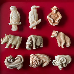 Pode incluir: Nove pequenas estatuetas de cerâmica de vários animais, incluindo um rinoceronte, um hipopótamo, um leão, um urso, um macaco, um pássaro e um carneiro. As estatuetas são pintadas em tons de marrom, branco e preto.