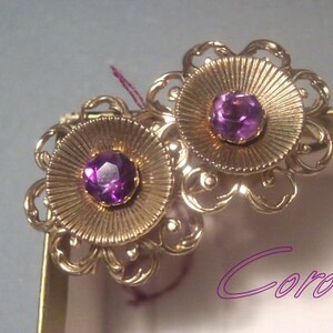May include: A pair of gold tone earrings with a floral design and purple gemstones. The earrings are marked "Coro".