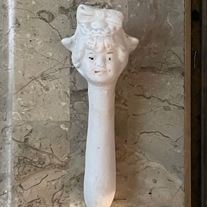 May include: White porcelain door handle shaped like a girl's head with a bow in her hair.