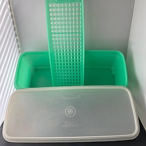 May include: A green rectangular Tupperware container with a matching lid and a green grid insert. The lid is translucent and has the Tupperware logo. The container is designed for food storage.