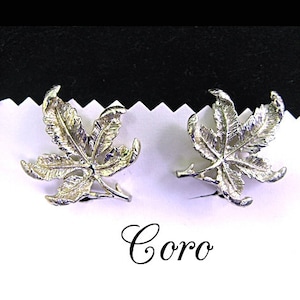 May include: A pair of silver tone Coro earrings featuring a detailed leaf design. The earrings are marked "Coro" on the back.