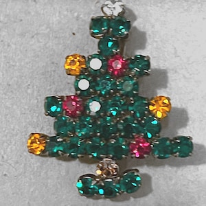 May include: A Christmas tree brooch, adorned with green, red, white, and yellow gemstones. The brooch features a festive tree design, crafted from small, glittering stones. A seasonal accessory, perfect for the holidays.