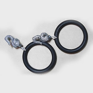 May include: Two black rubber rings with silver snake-shaped clasps. The clasps are detailed with small, clear stones.