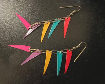 May include: A pair of dangle earrings with a chain of colorful triangular pendants. The pendants are in shades of pink, purple, yellow, blue, and red.