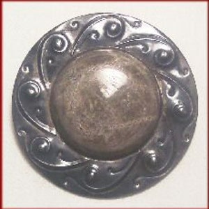 May include: A silver-toned button with a raised, circular center and a decorative, swirling design around the edge.