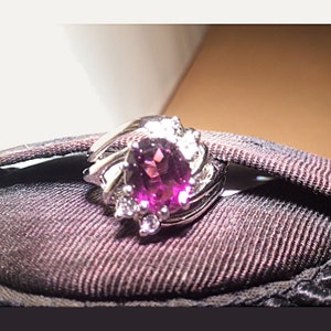 May include: A silver ring with a large oval-shaped purple gemstone surrounded by smaller clear gemstones.