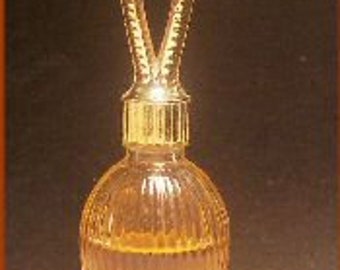 May include: A clear glass bell-shaped bottle with a gold-colored handle. The bottle has a ribbed design and is filled with a light amber liquid.
