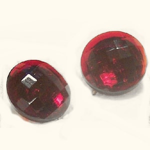 May include: A pair of red, faceted, oval-shaped earrings. The earrings are made of glass or plastic and have a shiny finish.